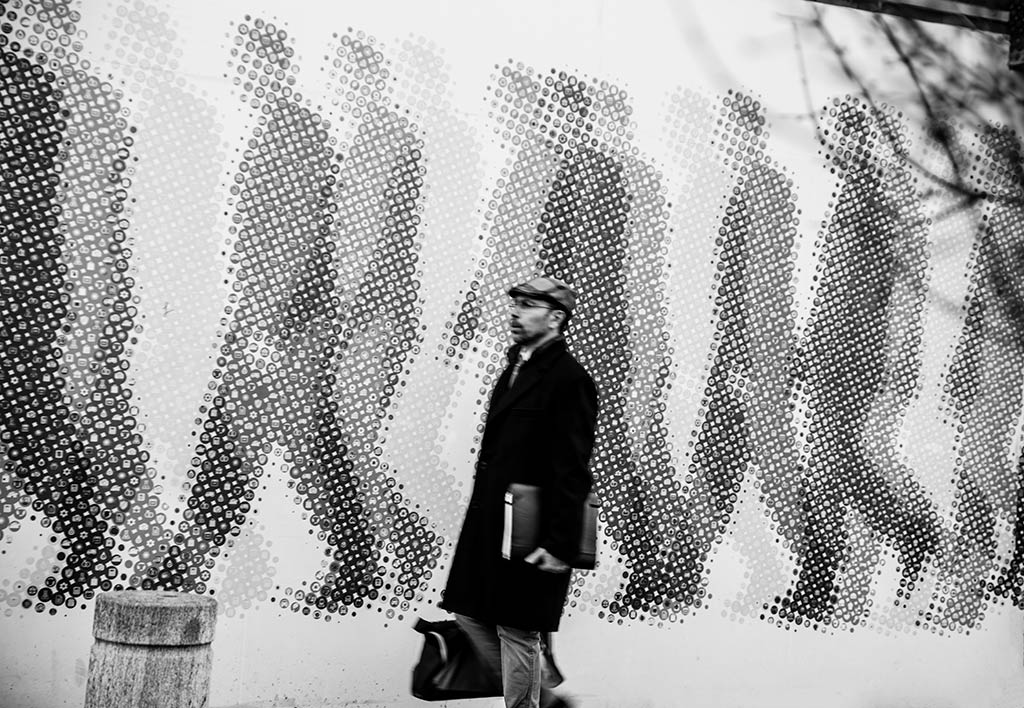 Milano: una curiosa foto ritrae un uomo in movimento sullo sfondo di un murales con persone in movimento