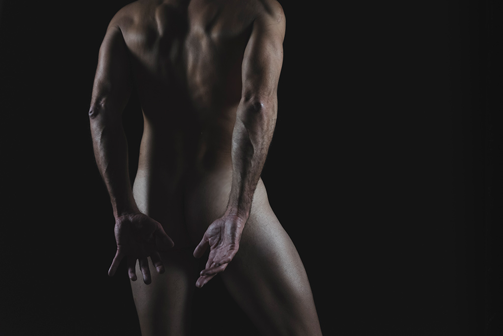 Hands - Il corpo a zone: un uomo nudo ripreso di spalle copre le natiche con le sue mani