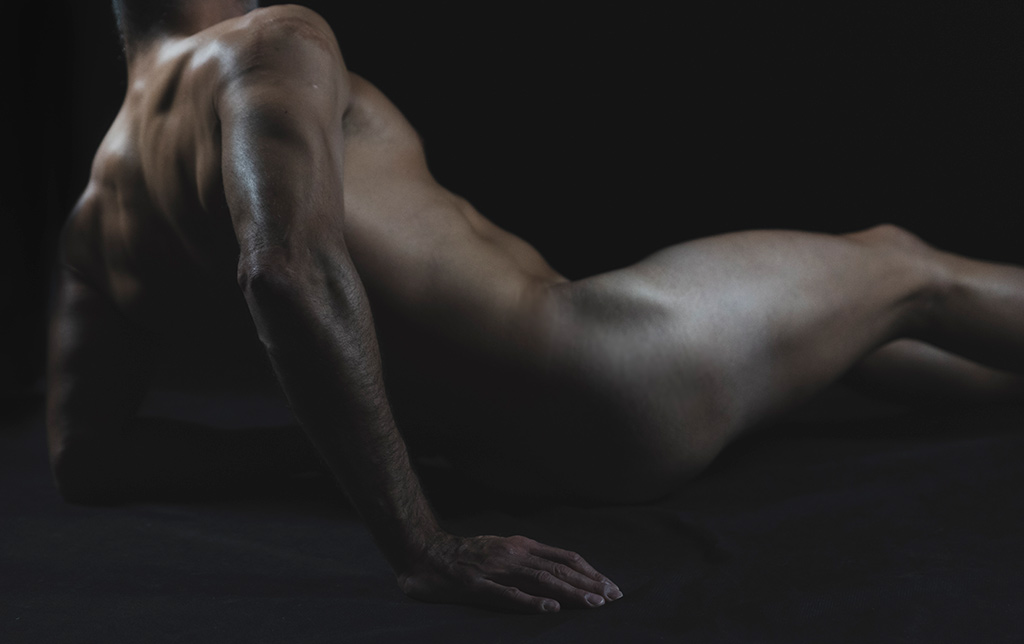 Hands - Il corpo a zone: un uomo nudo sdraiato di spalle mostra la possanza della sua muscolatura sorreggendosi