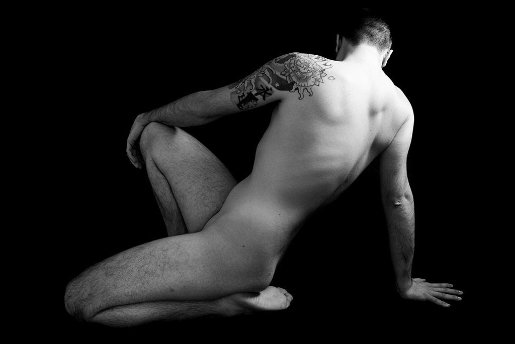 Raccoglimento: un uomo nudo mostra di spalle un tatuaggio sul braccio sinistro